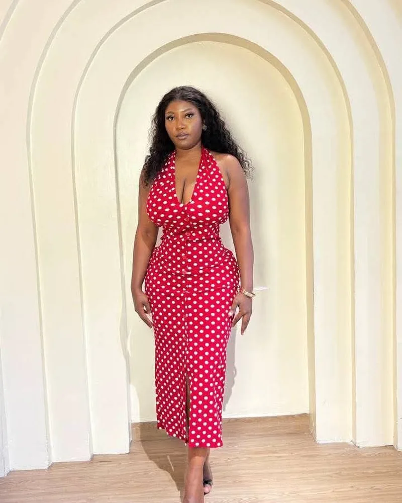 Robe longue rouge à pois, col licou, sous une arche crème